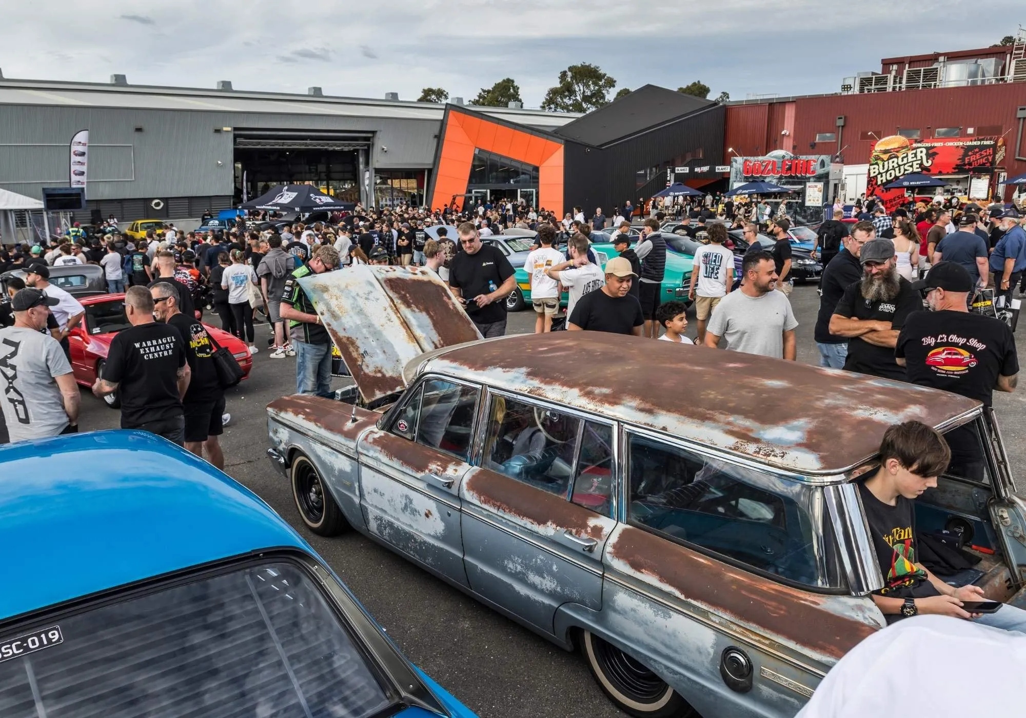 A patinated Holden wagon on display in Car Club World with crowds behind