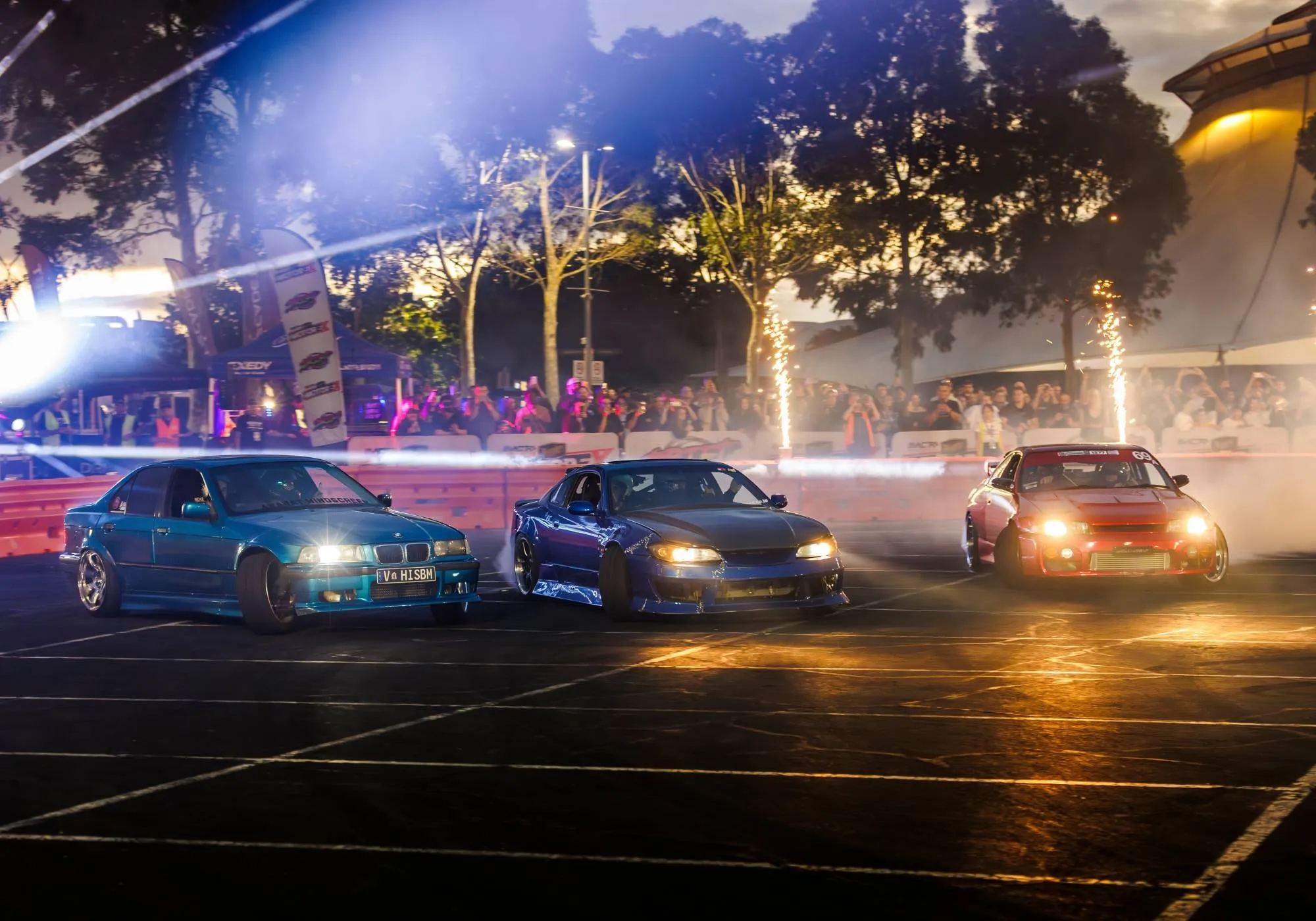 Three cars drifting in tandem under lights at Drift World
